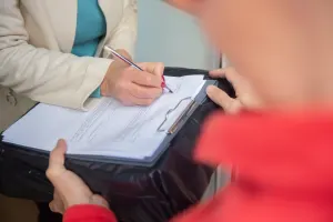 Woman signing a form as a man holds it for her