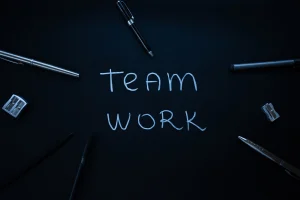 The words 'Team Work" written on a digital blackboard with writing implements and other office supplies around it