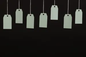 About half a dozen blank white tags hanging from above in front of a dark background