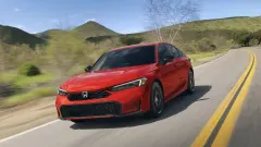 Red Honda Civic hybrid sedan on two lane road with green hills in background