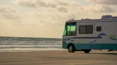 Blue and white RV parked on beach facing the ocean.