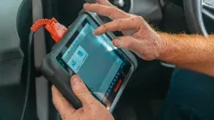 Mechanic's hand on digtial device screen next to a car