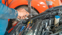 pair of hands holding tools working on a vehicle under the hood