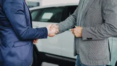 Two businessmen shaking hands in front of a vehicle