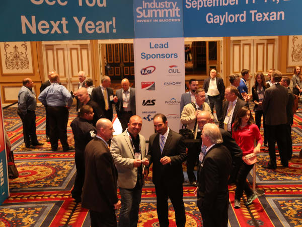 Attendees networking and talking in a conference hall beneath signage for the Industry Summit with sponsor displays in the background.