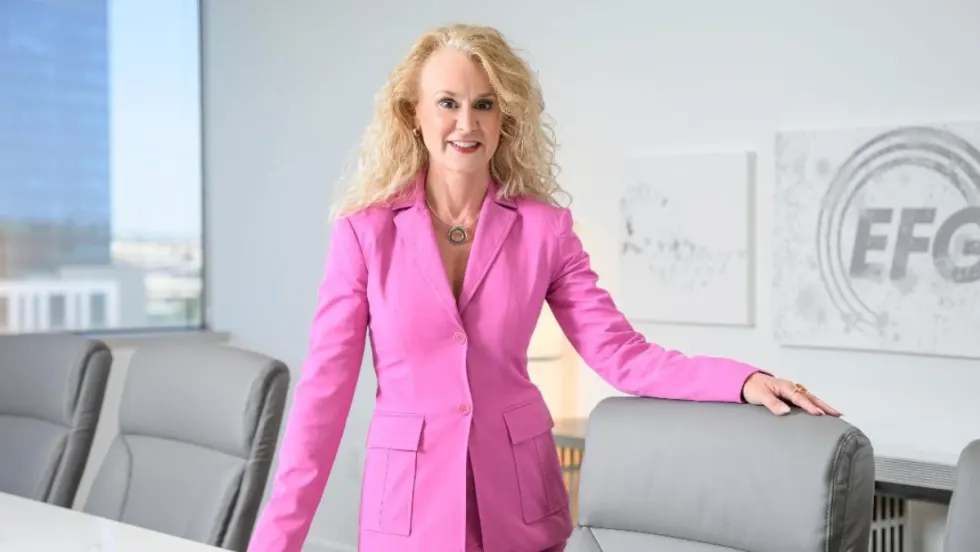 Jennifer Rappaport, CEO of EFG Companies, stands in a conference room wearing a bright pink suit, with the EFG logo visible on the wall behind her.
