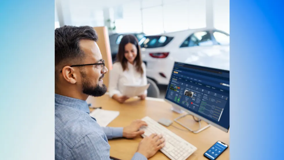 A car dealership employee uses Dealer Wizard’s equity-mining platform on a desktop computer while a customer reviews paperwork in the background.