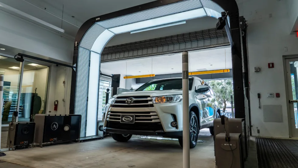 A white Toyota Highlander drives through a UVeye automated vehicle inspection system inside a dealership service area, part of Cox Automotive’s vAuto integration for faster appraisals.