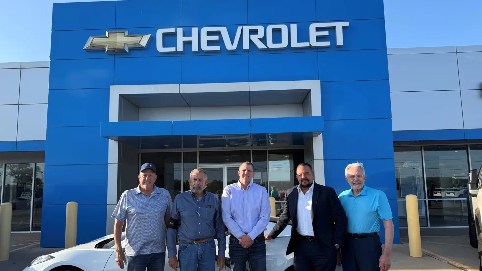 Photo of four men involved in sale of three auto dealerships, standing in front of the sold Chevrolet store