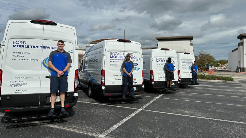 Photo of three Ford mobile service vans parked in lot with a technician standing at the back of each