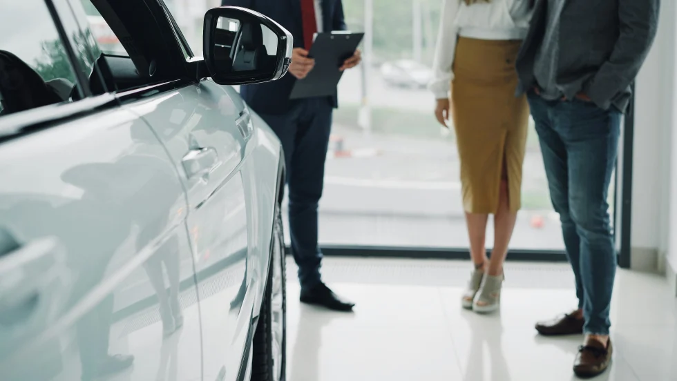 Couple talking with auto salesman next to new car inside dealership