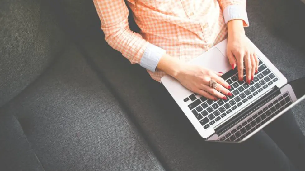 Photo of woman typing on a laptop as she sits on a couch