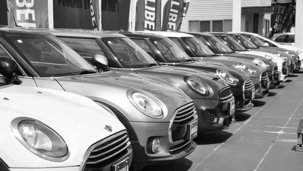 Gray-scale photo of a line of Mini cars in a dealership parking lot