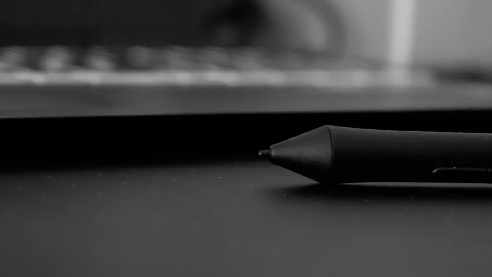 Photo of computer keyboard with a inkpen resting in front of it on the top of a desk