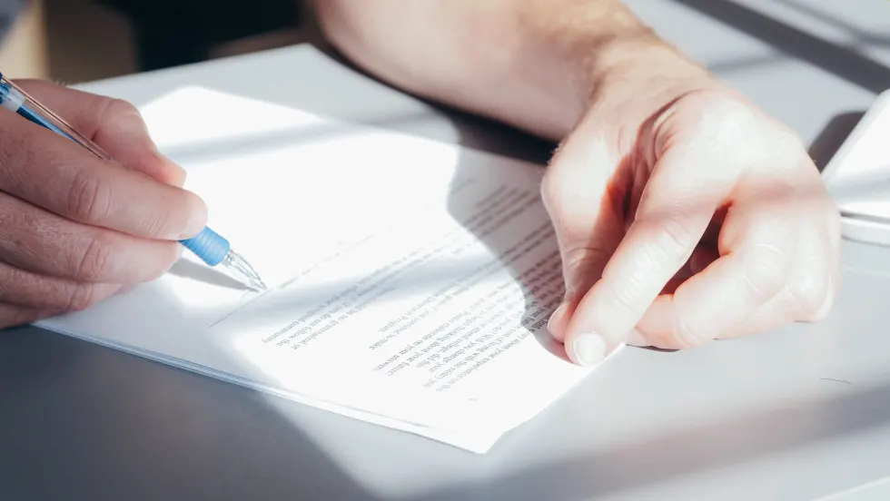 Photo of man signing document with a blue pen
