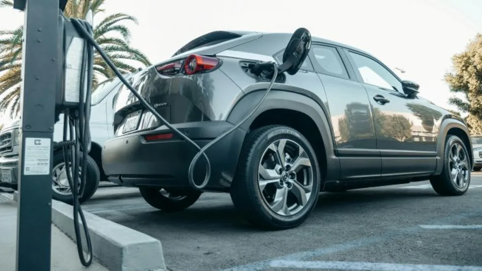 Photo of gray SUV plugged into public electric-vehicle charger in parking lot