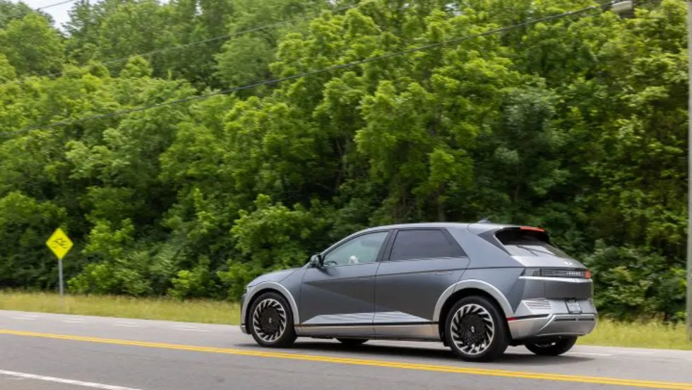 Photo of Ioniq 5 SUV moving on two-lane road next to treeline