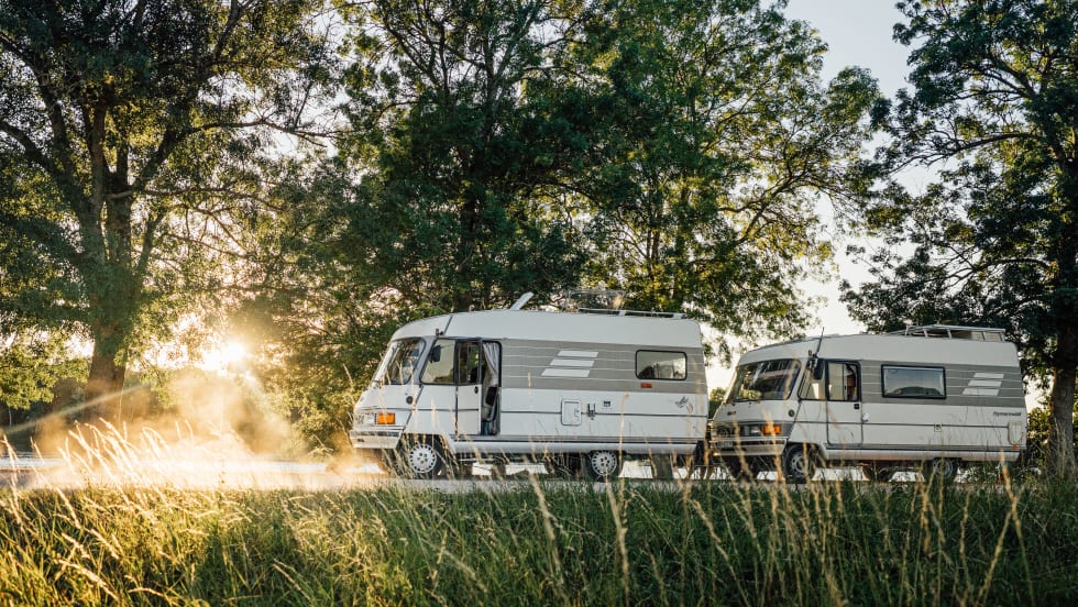 Two vans parked on road with scenic views behind.