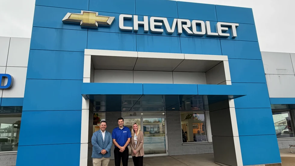 Two men and one woman standing in front of blue walled Chevrolet dealership entrance.