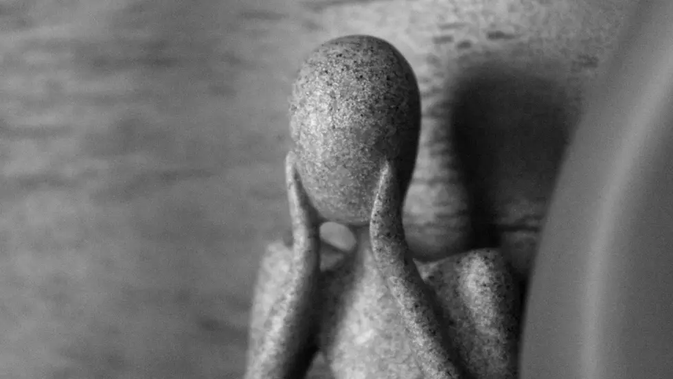 Marble statue holding hands to face.