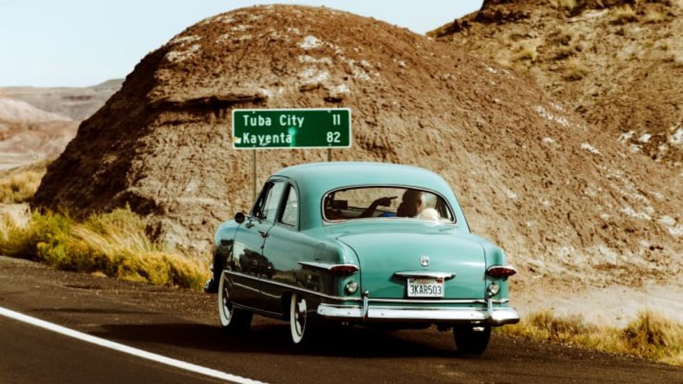 Teal antique car driving on road.