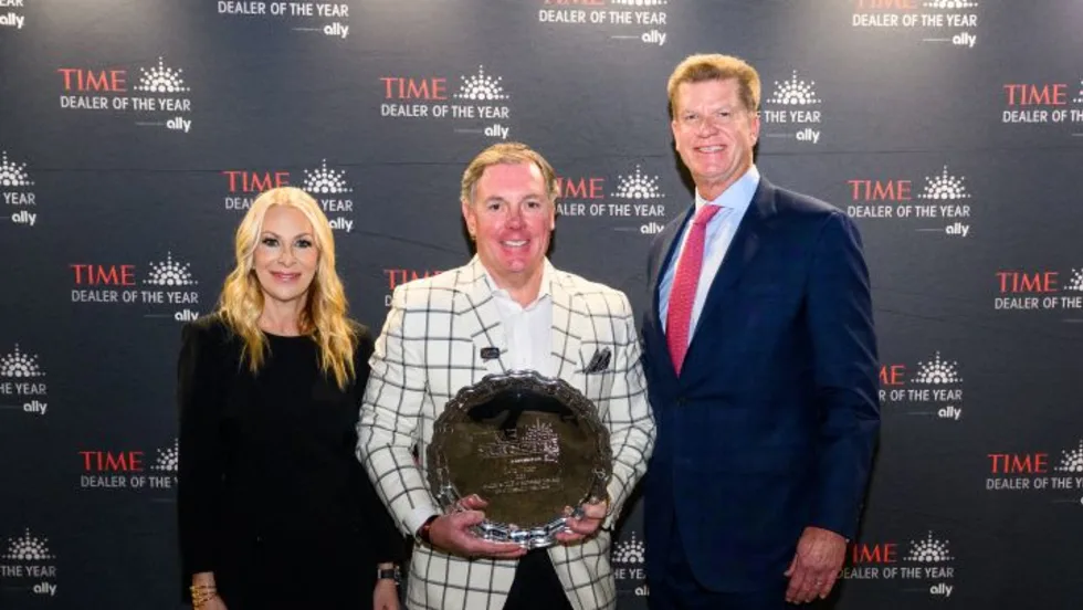 Two men and a woman smiling for photo while center man holds award