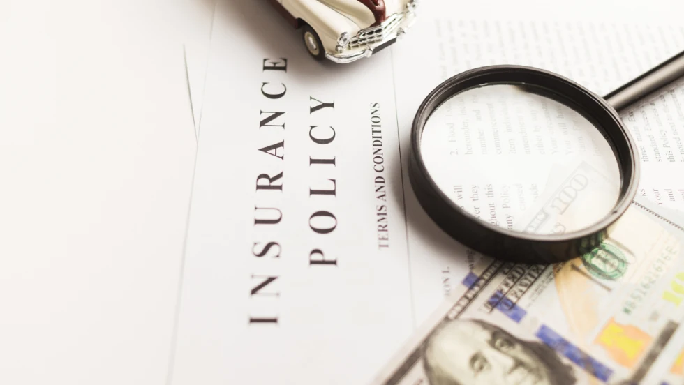 $100 bill and magnifying glass on top of paper that says insurance policy terms and conditions.