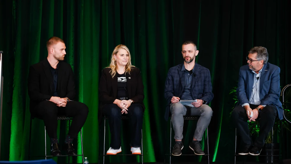 Three men and one woman sitting on a green backlit stage talking