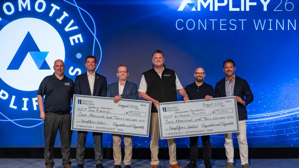 Six men standing on stage receiving two giant $5,000 checks.