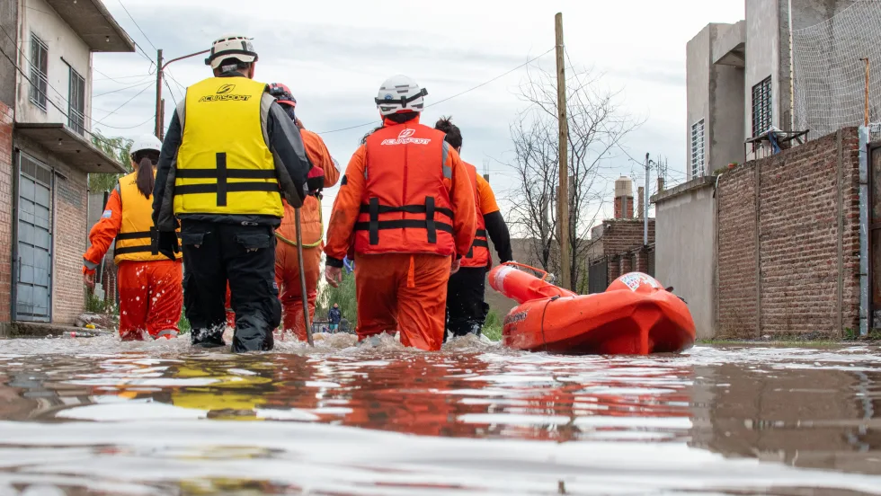 Disaster response team wading through knee deep water with life raft beside them.