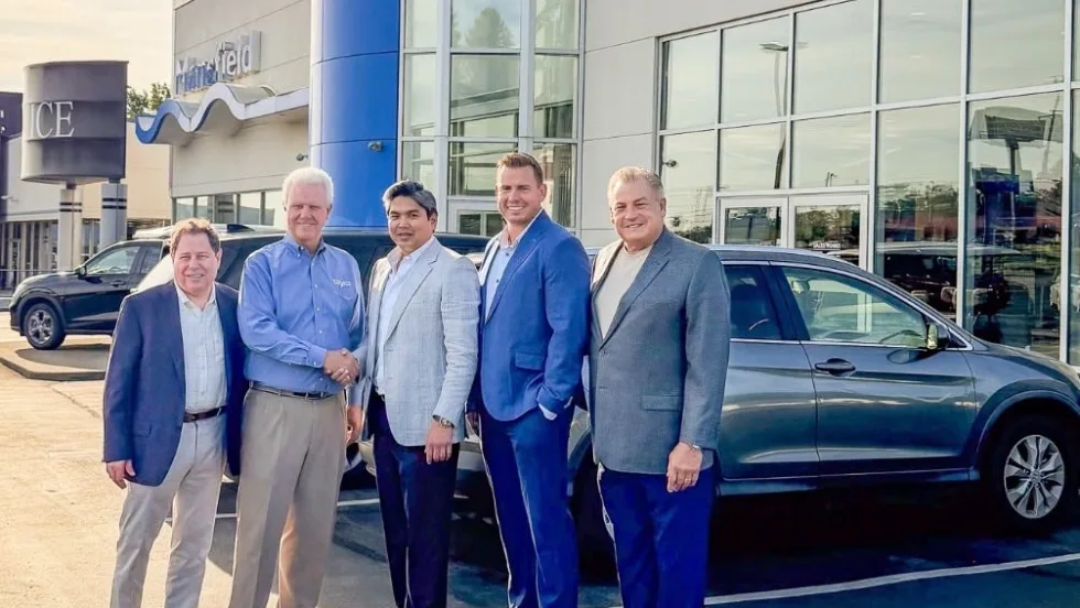 Five men smiling for photo in front of Honda car dealership.