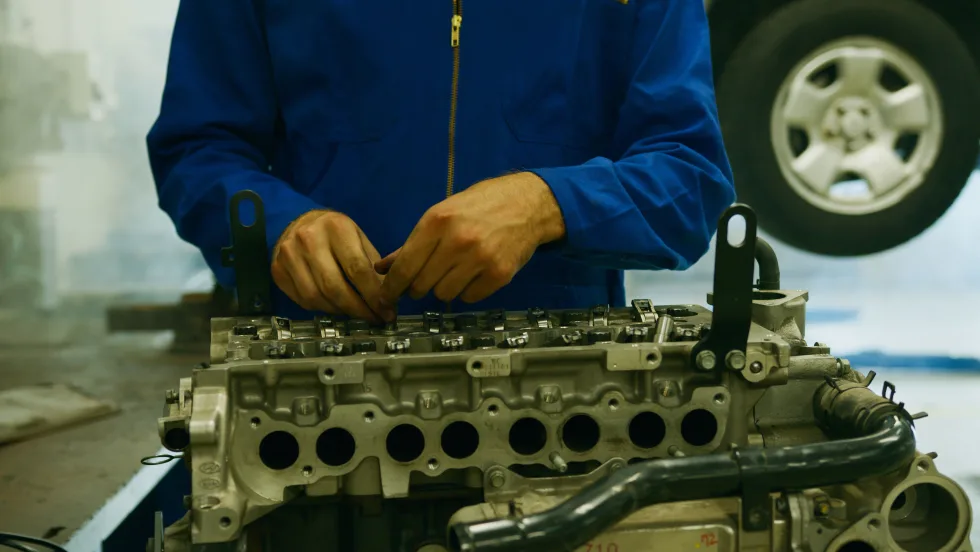 Photo of a mechanic working on an engine with a car on a lift in the background