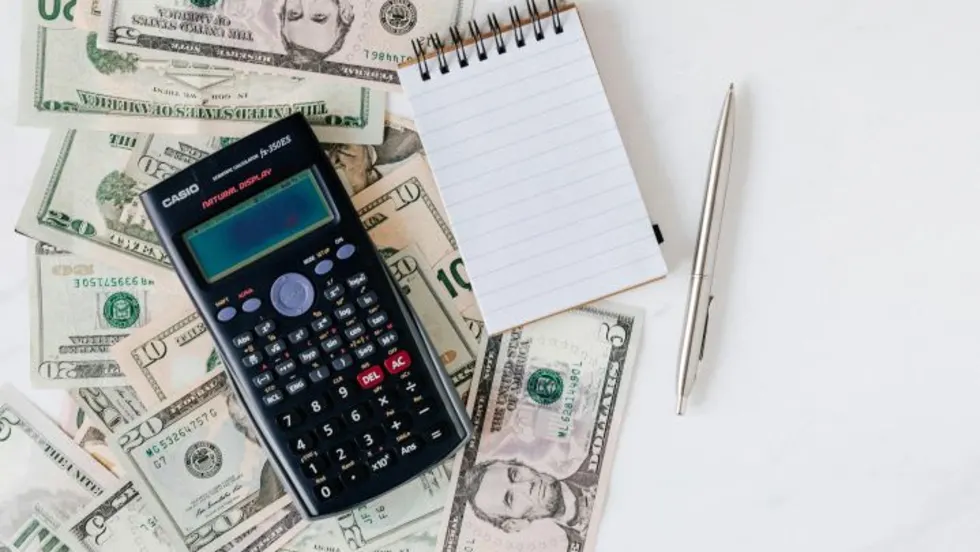 Photo of paper money bills, a calculator, notepad and pen