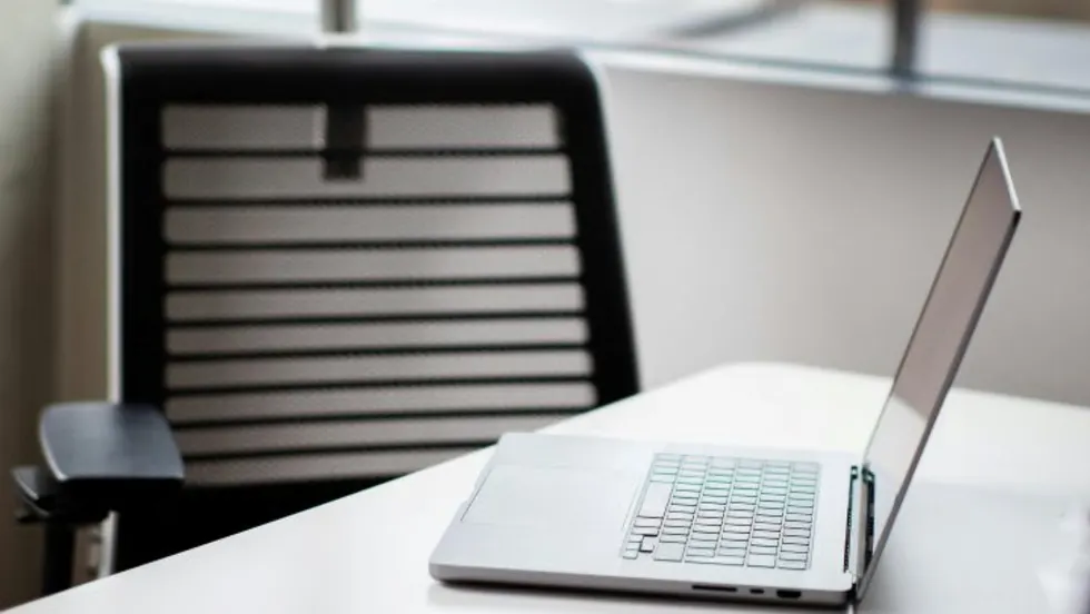 Laptop computer open on desk with empty chair behind it