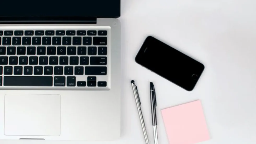 Photo of laptop on desk with pens, phone and sticky notepad beside it