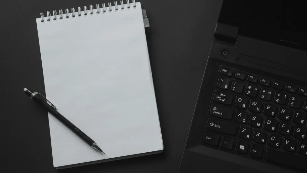 Photo of notepad and pen next to computer keyboard on desktop