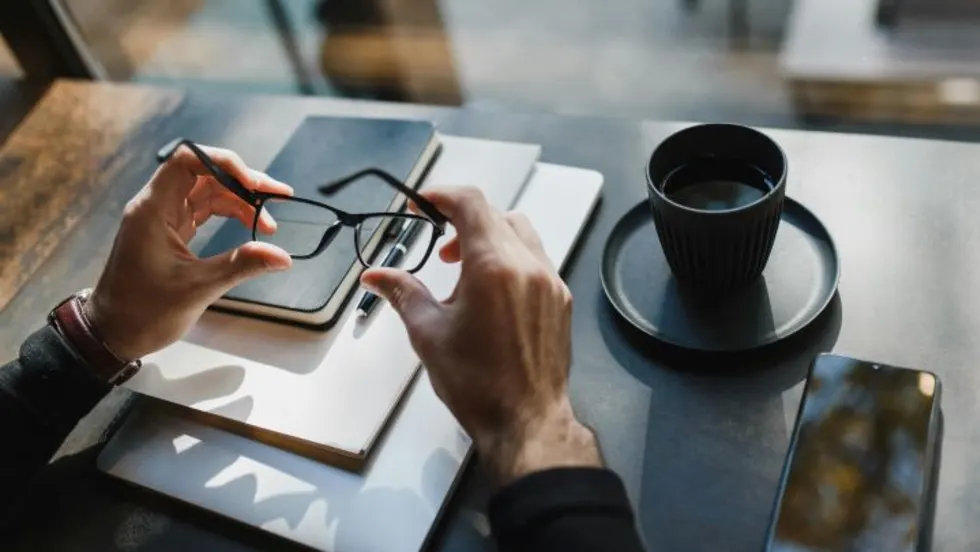 Photo of businessman's hands holding eyeglasses at a desk