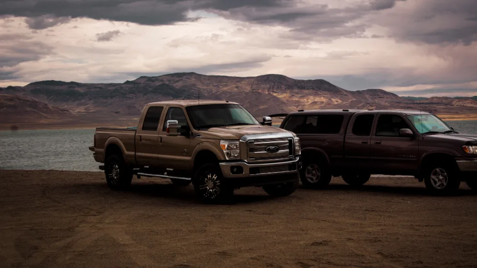 outside shot of two trucks in front of a body of water with a cloudy sky
