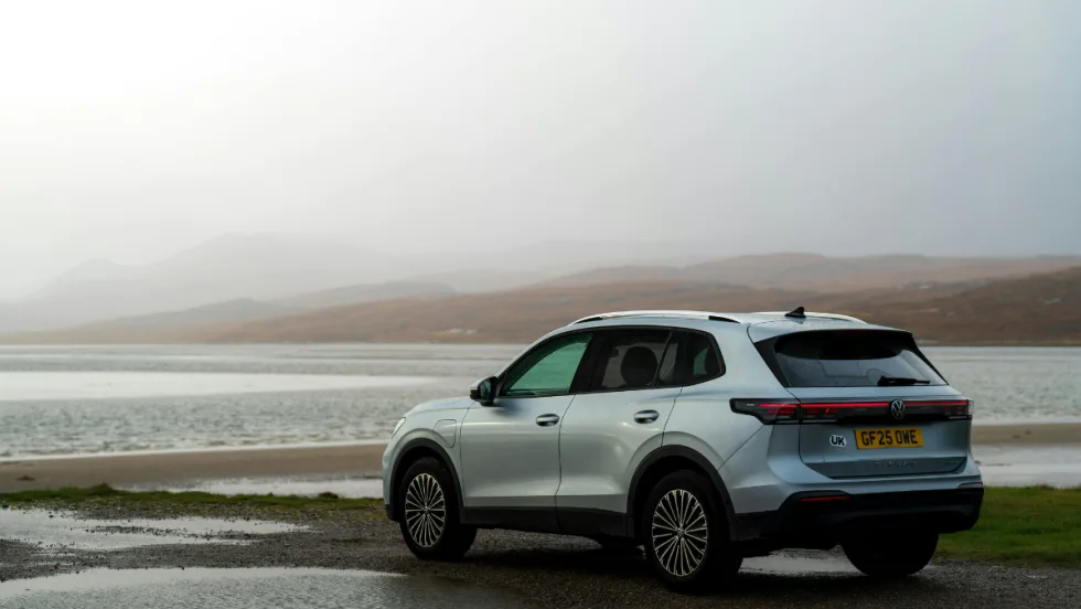 white SUV parked in front of a body of water with a gray sky background