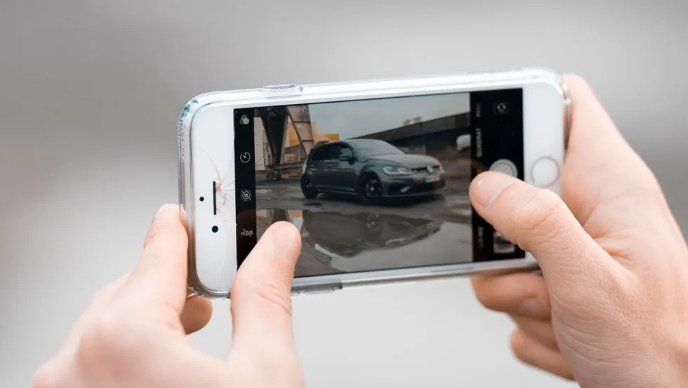 hands holding up a phone horizontally, zooming into a picture of a car