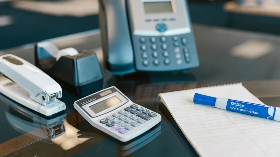 Photo of an land-line phone on a desk with various office supplies