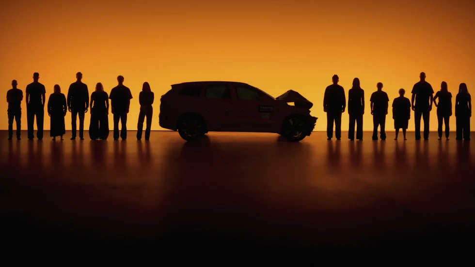 orange background behind a line of people with a crashed car in the middle