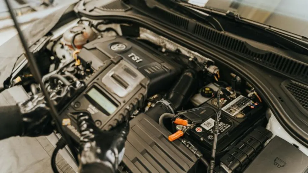 Mechanic holding a vehicle diagnostic device while standing above an open car hood