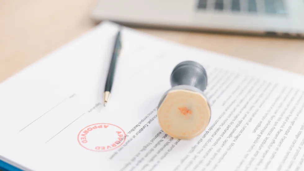 white document with black text, stamp laying on top with red circle stamp of approval on top of paper