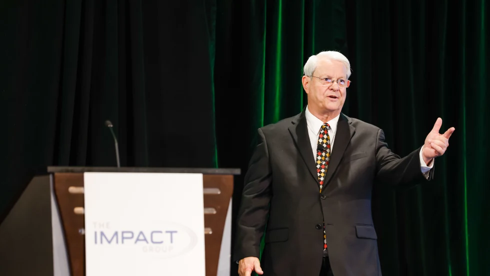 man with white hair and glasses delivering a speech standing next to a podium