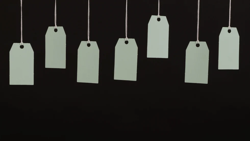 About half a dozen blank white tags hanging from above in front of a dark background