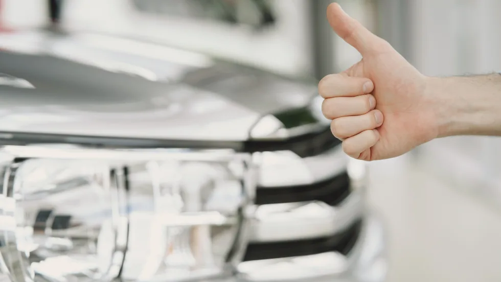 car in background with hand giving a thumbs up in front