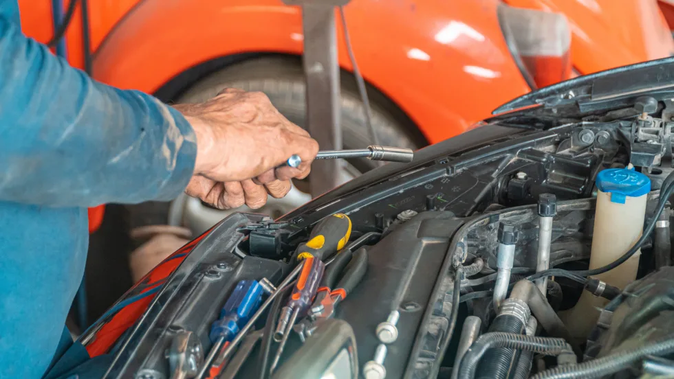 pair of hands holding tools working on a vehicle under the hood