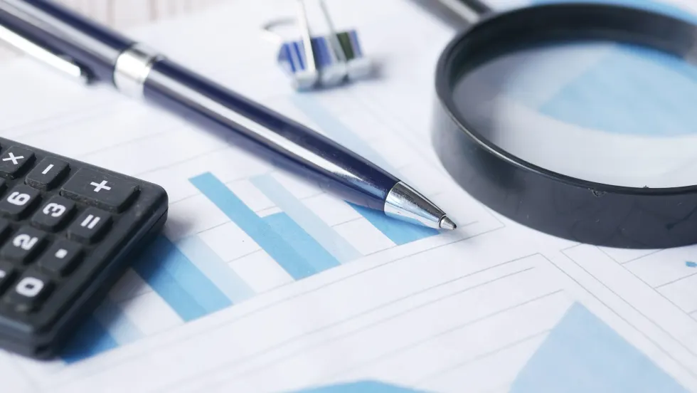 Photo of financial documents with a magnifying glass, calculator and pen on top