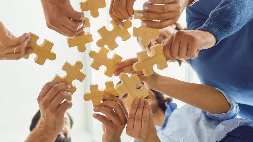 group of people standing in a circle holding puzzle pieces together